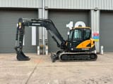 2023 Hyundai HX85A Mini Excavator from a side view, highlighting the full length of the dark grey tracks.