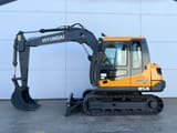 2026 Hyundai R85A Crawler Excavator with its orange body and dark gray boom extended to the left, showing the digging bucket.